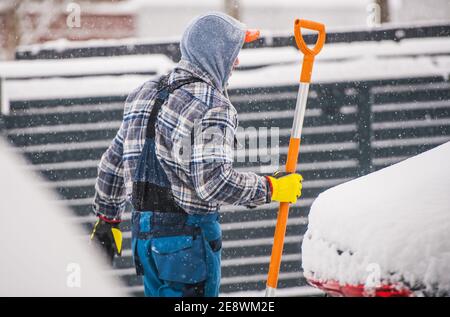 Kaukasische Männer in seinen 40er Jahren Entfernen von Schnee während schwerer Schneefall mit großen Schnee Schaufel. Stockfoto