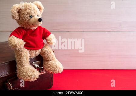 Reisekoffer und niedlicher Teddy sitzen auf rotem Boden. Kind hat das Konzept aufgegeben. Ledergepäck im Kinderzimmer Stockfoto