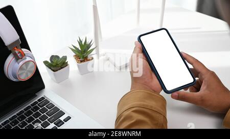 Nahaufnahme eines Mannes, der am Arbeitsplatz mit einem Laptop und einem Wireless-Router Smartphone in der Hand hält. Stockfoto