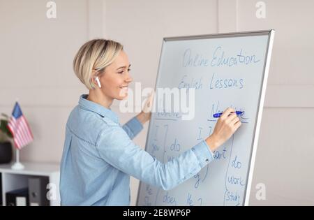 Glücklicher Lehrer, der englische Grammatikregeln auf Tafel schreibt und online Fremdsprachenunterricht von zu Hause aus durchführt Stockfoto