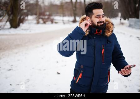 Bart indischen Mann tragen Jacke in kalten Wintertag. Er spricht Mobiltelefon über kabellose Kopfhörer. Stockfoto