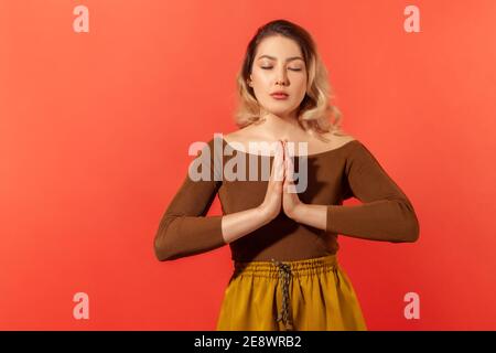 Porträt einer ruhigen blonden Frau stehend, nahm die Hände zusammen, beten oder Gleichgewicht mit Yoga-Training und geschlossenen Augen. Meditation und konzentrierte sie Stockfoto