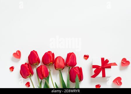 Valentinstag Romantische Hintergrund. Rote Tulpen, ein Geschenk mit Schleife und Kerzenherzen auf weißem Hintergrund mit Kopierraum. Flach liegend Stockfoto