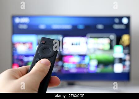 Männliche Hand mit Fernbedienung auf Smart TV-Bildschirm Hintergrund. Person, die Streaming-Dienste wählt, Filme ansieht Stockfoto