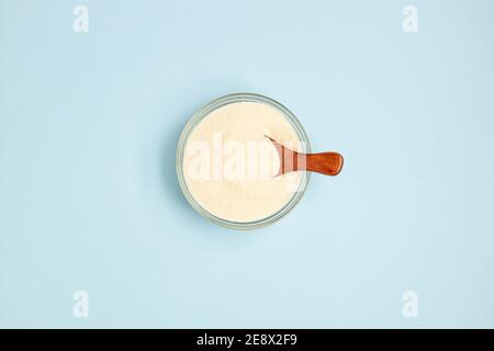 Draufsicht auf Kollagenpulver oder Protein im Glas Schüssel und ein kleiner Holzlöffel auf blauem Hintergrund Mit einem Kopierbereich Stockfoto