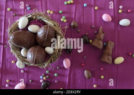 Draufsicht auf das Nest mit Schokoladeneiern, Schokoladenkaninchen und ostermandeln auf dem Tisch Stockfoto