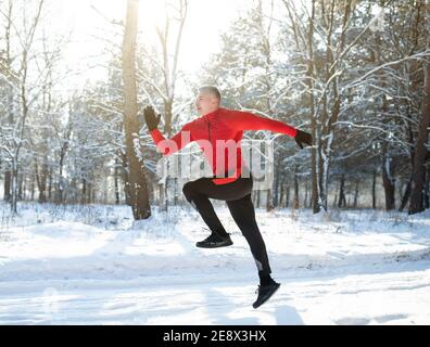 Ganzkörperportrait eines starken, reifen Sportlers, der draußen im sonnigen Winterpark joggt. Saisonale Sport und Aktivitäten Stockfoto