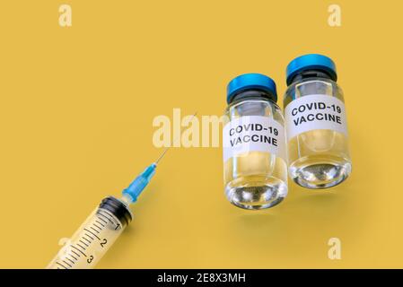 Coronavirus-COVID-19-Impfstoff. Fläschchen mit Spritze isoliert auf gelbem Hintergrund, Konzeptkomposition mit Kopierraum in der Draufsicht Stockfoto
