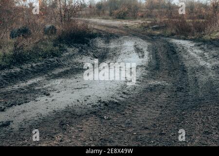 Schmutzige gebrochene Straße von großen Gummireifen von Auto, Traktor und Tank. Schmutzige flüssige Pfütze nach Regen an der Basis der Saison Stockfoto