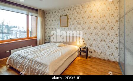 Modernes Interieur des Schlafzimmers in Luxus-Wohnung. Gemütliches Bett. Riesiges Fenster. Lampen an Nachttischen. Stockfoto