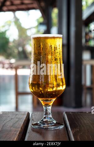 Ein Glas kaltes Bier Bernstein Farbe mit Kondenswasser auf einem Holztisch in einem Pub, Bar. Alkoholgetränk. Sommerfreizeitkonzept Stockfoto