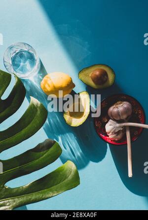 Zutaten für frisches mexikanisches Guacamole, zwei Avocado-Hälften, Knoblauch und Limette/Zitrone isoliert auf türkisblauem Hintergrund Stockfoto