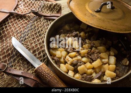 Venisenstücke von einem Damhirsch, die mit gewürfeltem Lamm gebraten und mit Kartoffeln und Knoblauch gekocht wurden. Serviert in einer Kupferpfanne neben einem Stockfoto