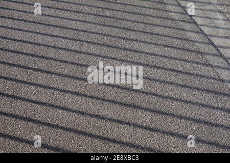 Der Schatten eines Zauns auf einer Fußgänger-Wanderung. Grauer Hintergrund auf Asphalt erstellt. Stockfoto