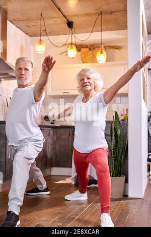 Senior-Paar in Krieger Yoga Pose, tun Virabhadrasana zu Hause zusammen, sportliche Mann und Frau Stockfoto