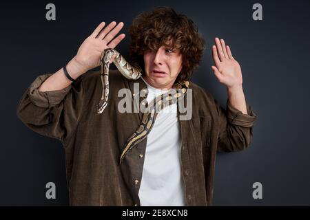 Weinende Männchen hat Angst vor Schlange, die um seinen Hals wickelt, stehen schreien isoliert auf schwarzem Hintergrund Stockfoto