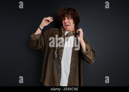 Weinende Männchen hat Angst vor Schlange, die um seinen Hals wickelt, stehen schreien isoliert auf schwarzem Hintergrund Stockfoto