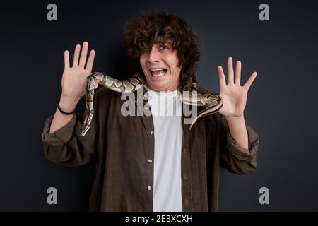 Weinende Männchen hat Angst vor Schlange, die um seinen Hals wickelt, stehen schreien isoliert auf schwarzem Hintergrund Stockfoto