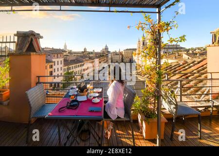 Eine junge Brünette sitzt nach einem Essen an einem Tisch auf dem Dach und genießt den Blick auf die Piazza Navona in Rom, Italien Stockfoto