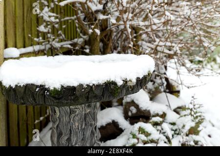 Nahaufnahme eines mit Stein verzierten Vogelbades, das mit Schnee bedeckt ist Draußen in einem heimischen Garten an einem kalten Wintertag Stockfoto