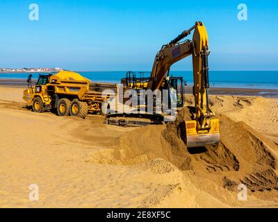 Mechanischer Bagger und Erdschlepper Entfernung Sand vom Strand in Colwyn Bay Conway Wales Großbritannien nach schweren Winterstürmen verdrängte den Sand. Stockfoto