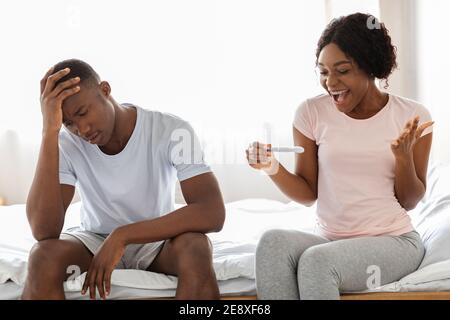 Glückliche schwarze Frau mit Schwangerschaftstest und ihr unglücklicher Freund Stockfoto