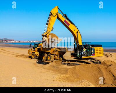 Mechanischer Bagger und Erdschlepper Entfernung Sand vom Strand in Colwyn Bay Conway Wales Großbritannien nach schweren Winterstürmen verdrängte den Sand. Stockfoto