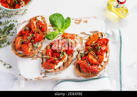 Sandwiches mit gebackenen Kirschtomaten und Quark, Thymian, Knoblauch und Kräutern auf einem alten leichten Vintage-Hintergrund. Frühstückskonzept. Draufsicht. Stockfoto