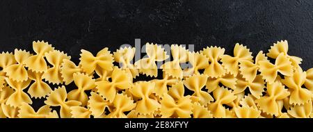 Farfalle rohe Pasta auf schwarzem Beton Hintergrund. Kochkonzept. Draufsicht mit Kopierbereich. Stockfoto