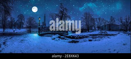 Magische Winternacht mit Sternenhimmel und Vollmond in verschneiten Park mit schöner Brücke über kleinen Teich, Straßenlicht und mit Schneebäumen bedeckt. Stockfoto