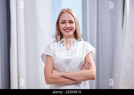 Krankenschwester in weißem Mantel Blick auf Kamera stehend mit Armen gefaltet, Arzt Praktizierende Frau posiert und lächelt, Medizin und Gesundheitswesen conce Stockfoto