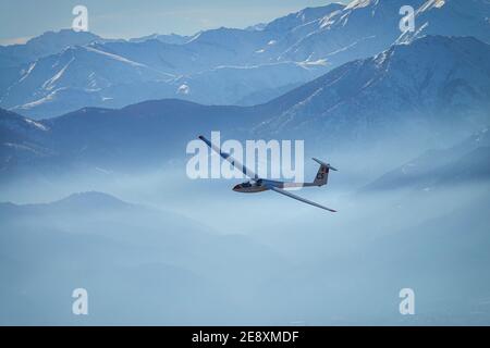 Segelflugzeug im Flug zwischen verschneiten Bergen von oben gesehen. Susa, Italien - Januar 2021 Stockfoto