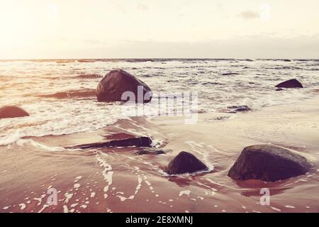 Farbiges Bild von Felsen am Strand bei goldenem Sonnenuntergang. Stockfoto
