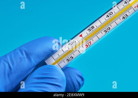 Person in medizinischen Handschuhen hält Quecksilberthermometer, die 37 Temperatur zeigen. Fieber Konzept Stockfoto