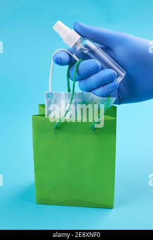 Person Hand in medizinischen Handschuhen hält Einkaufs-oder Vorratsbeutel mit Gesicht medizinische Maske und antiseptisch. Covid-19 Stockpiling Konzept. Pandemie Essentials Set Stockfoto