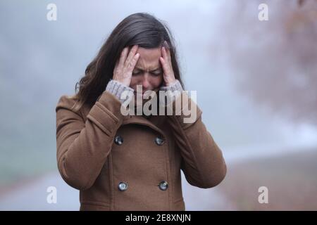 Traurige Frau im Winter beschwert sich allein zu Fuß in einem Park Ein nebliger Tag Stockfoto