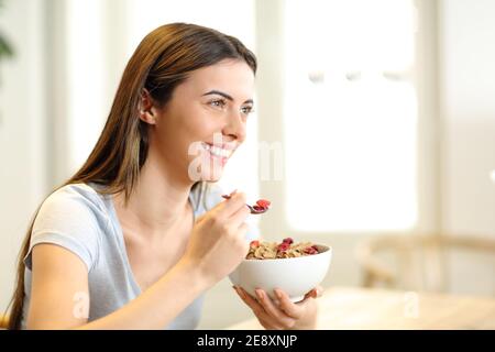 Glückliche Frau, die Müsli aus der Schüssel zum Frühstück im gegessen hat Wohnzimmer zu Hause Stockfoto