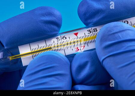 Person in medizinischen Handschuhen hält Quecksilberthermometer, die 37 Temperatur zeigen. Fieber Konzept Stockfoto