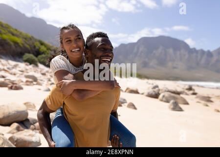 afroamerikanisches Paar Huckepack an einem Strand am Meer Stockfoto