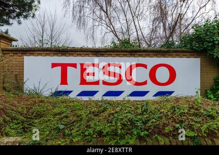 Mold, Flintshire; UK: Jan 28, 2021: Ein Schild mit der Werbung für den nahe gelegenen Tesco Supermarkt ist an einer Ziegelmauer befestigt und von Büschen umgeben Stockfoto