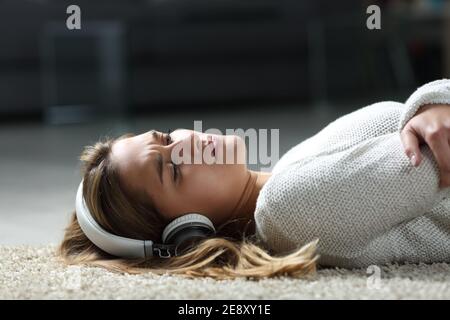 Traurige Frau, die Musik hört und Kopfhörer trägt, die auf dem liegen Boden zu Hause Stockfoto