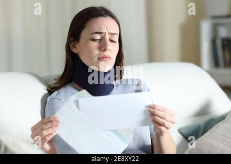 Traurige behinderte Frau, die schlechte Nachrichten auf dem Brief liest, auf dem sie sitzt Eine Couch im Wohnzimmer zu Hause Stockfoto