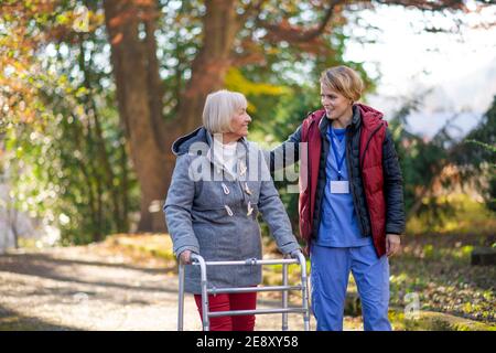 Ältere Frau mit Gehrahmen und Betreuer im Freien auf einem Spaziergang im Park. Stockfoto