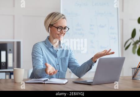 Erfahrene Englischlehrerin, die Online-Unterricht auf dem Laptop gibt, mit Schülern chattet, von zu Hause aus am Webinar teilnimmt Stockfoto