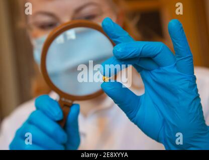 Ein Labortechniker in einem weißen Gewand und blauen Handschuhen Untersucht durch eine Lupe Stockfoto