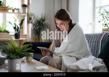 Verärgert junge Frau in Decke auf Sofa zu Hause eingewickelt, mit Tablet. Stockfoto