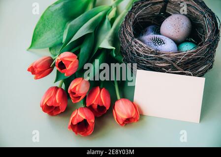 Bemalte Eier im Nest und ein Bündel Tulpen, Osterkonzept. Draufsicht, Mock up. Stockfoto