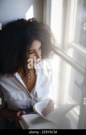 Porträt einer jungen Frau mit Buch drinnen zu Hause, Lesen. Stockfoto