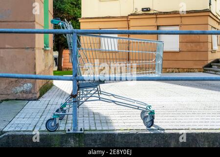 Ein gestohlener verlassener Supermarktwagen ist mit einem rostigen verkettet An einen Metallgeländer in einem alten Innenhof mit Ketten Abblätternde Wände mit Moos und geschlossen Stockfoto