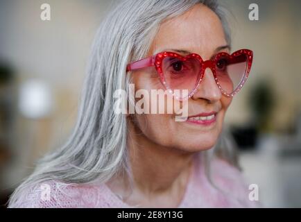 Porträt einer glücklichen älteren Frau mit Party-Sonnenanbeter, die zu Hause drinnen steht. Stockfoto